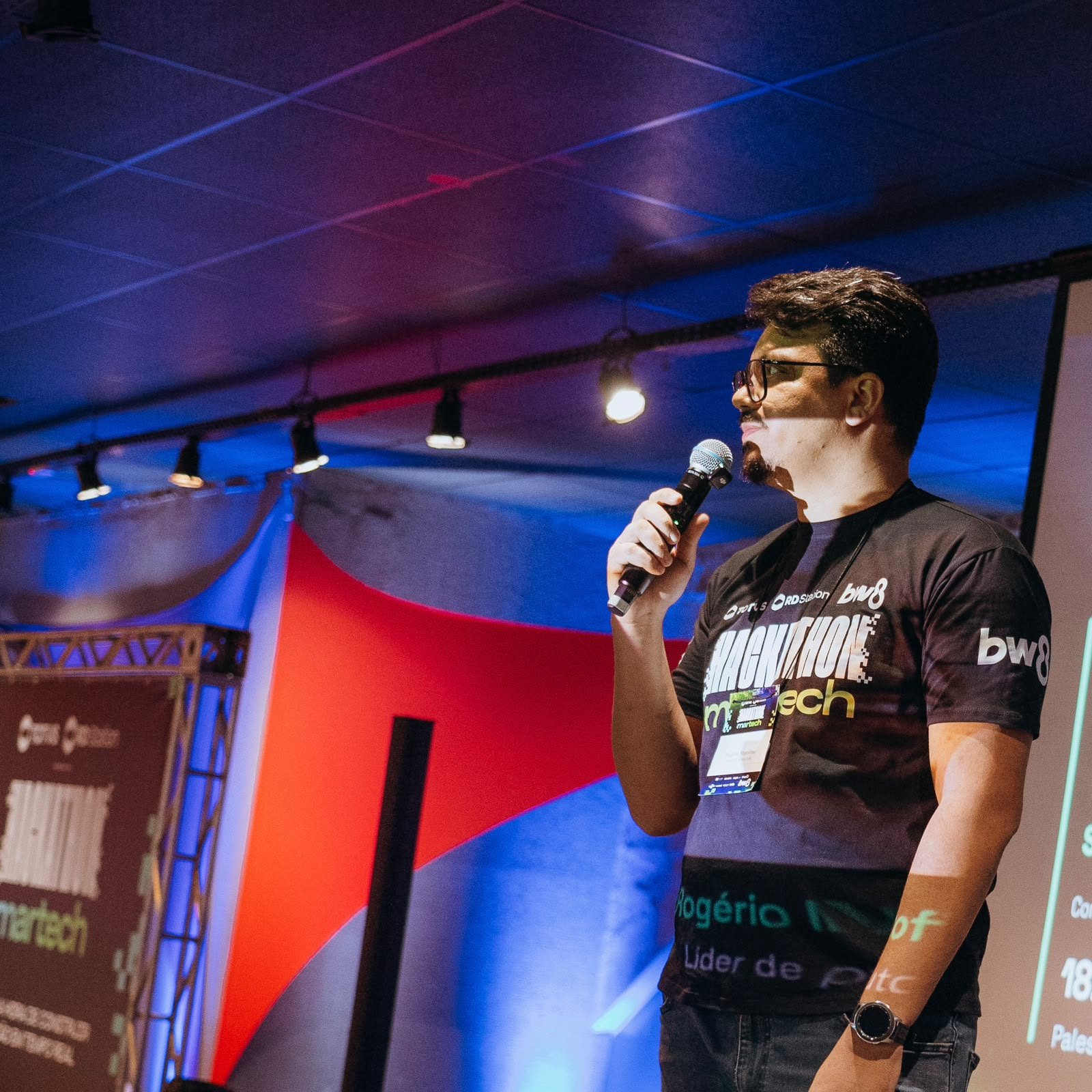 Rogério Matofino palestrando com microfone no palco do Hackathon Martech